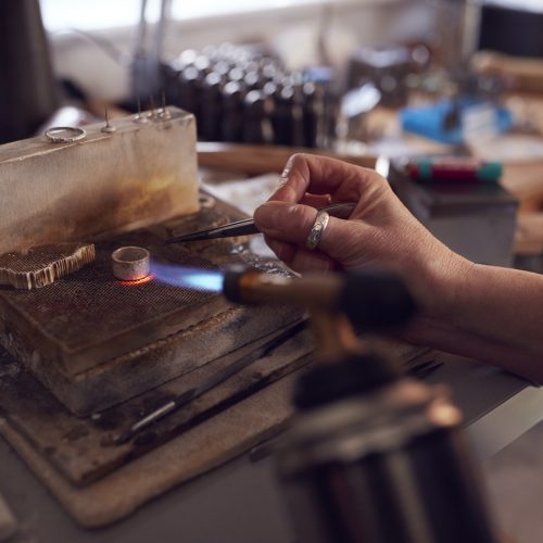 Close Up Of Male Jeweller Working On Ring With Blowtorch In Studio