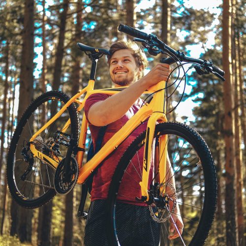 Positive sporty male holding yellow mountain bicycle.